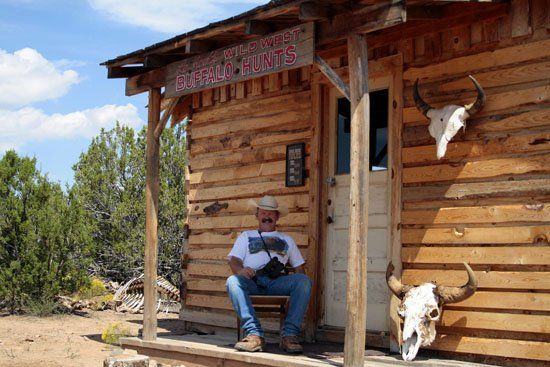 A man sits on a porch under a sign that says buffalo hunts