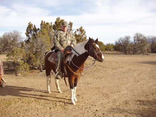 A man riding a brown and white horse in a dirt field
