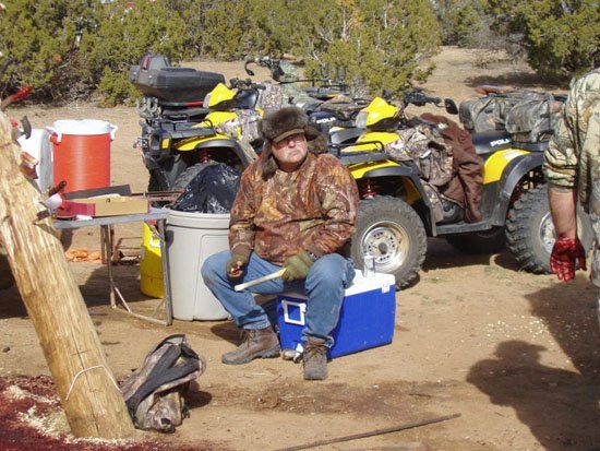 A man sits on a blue cooler in front of a row of four wheelers