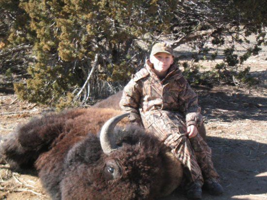 A boy in a camo jacket sits next to a bison
