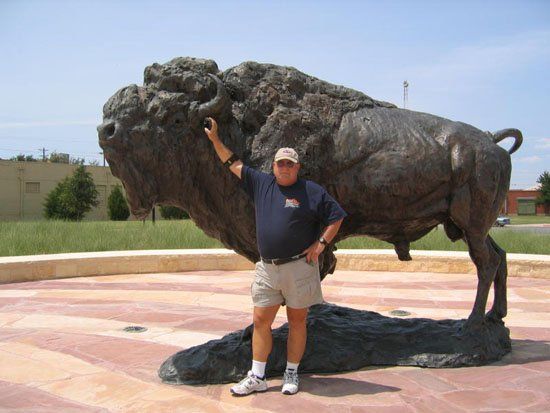 A man stands in front of a statue of a bison
