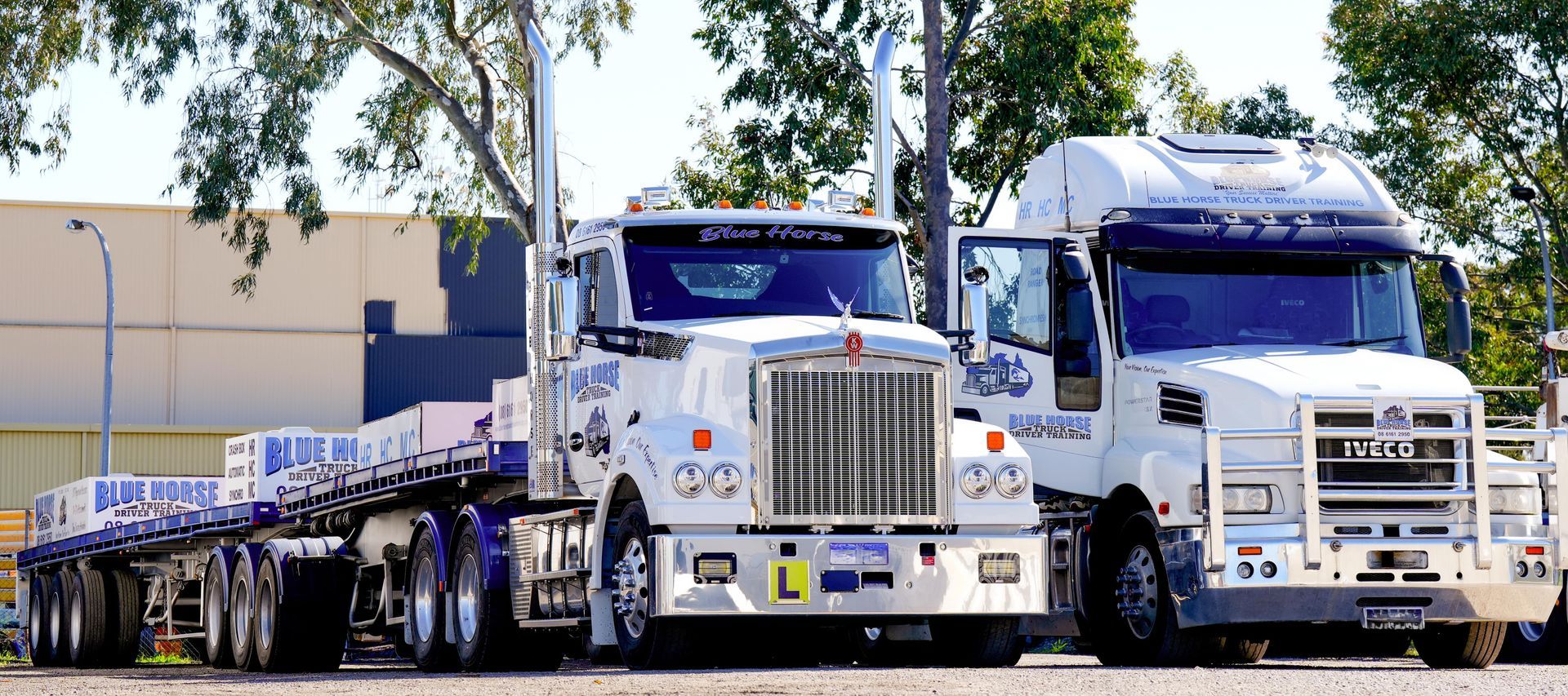 Two white semi-trucks parked side-by-side. One has a trailer. The other's door is open.