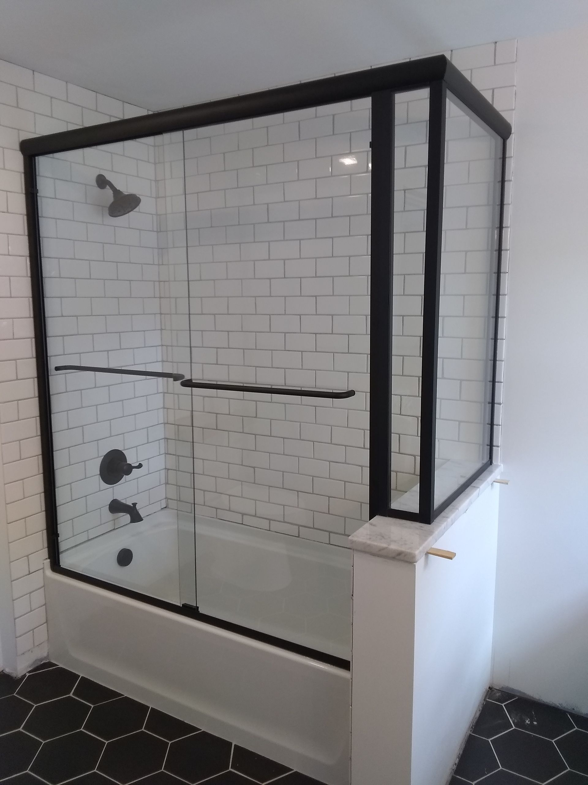 A bathroom with a bathtub and a shower with a black frame.