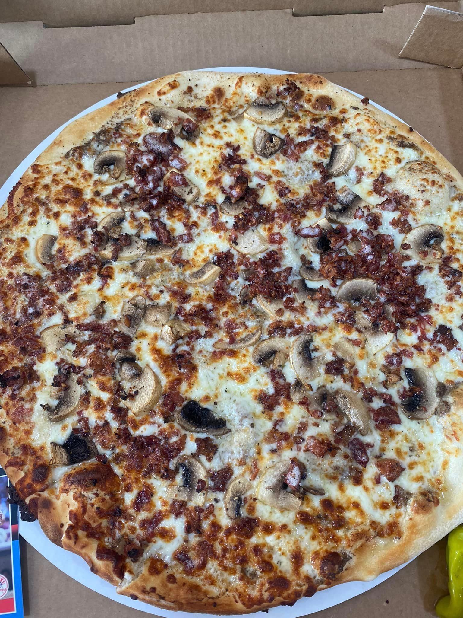 A pizza with mushrooms , bacon and cheese on a white plate in a box.