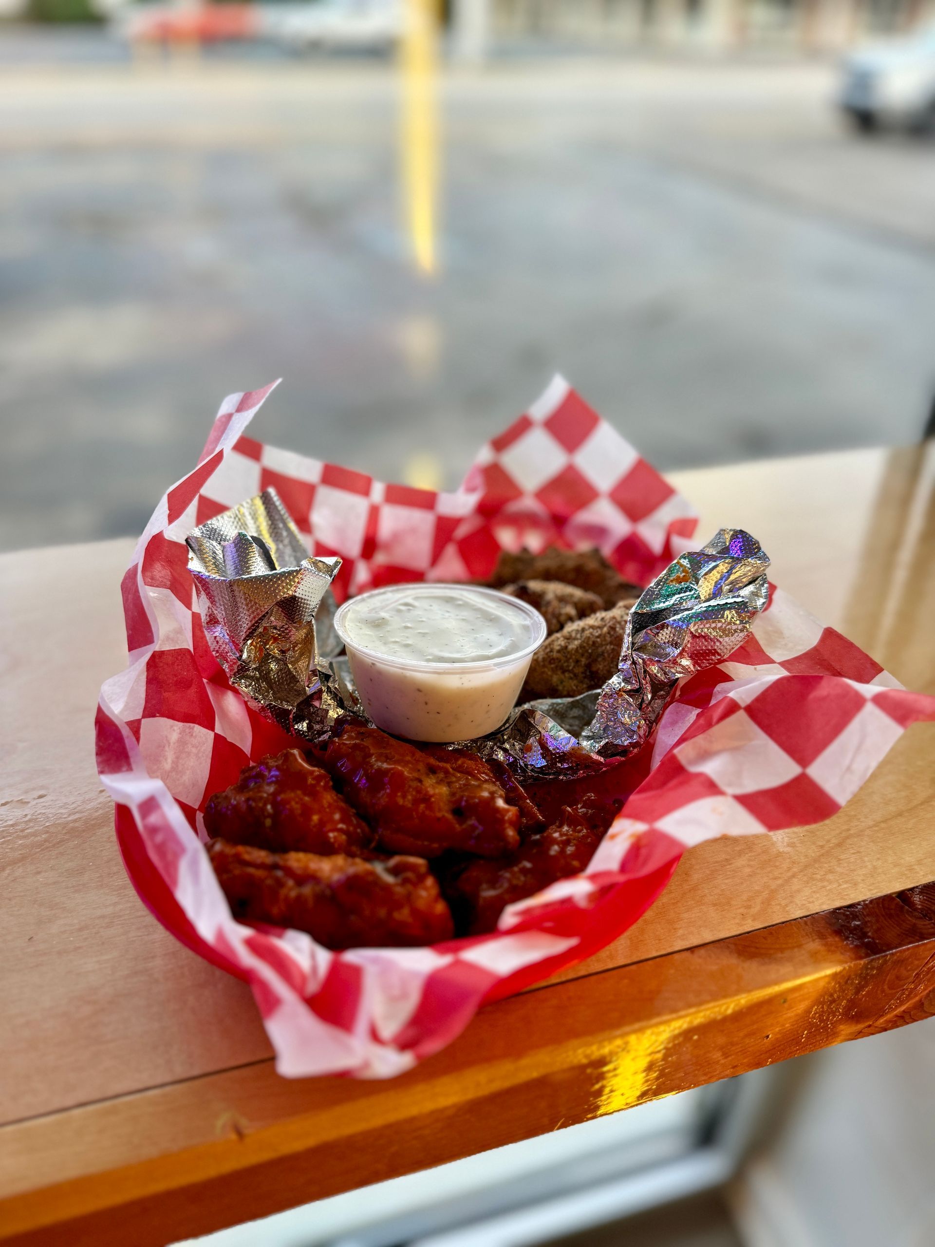 A basket of chicken wings with dipping sauce on a table.