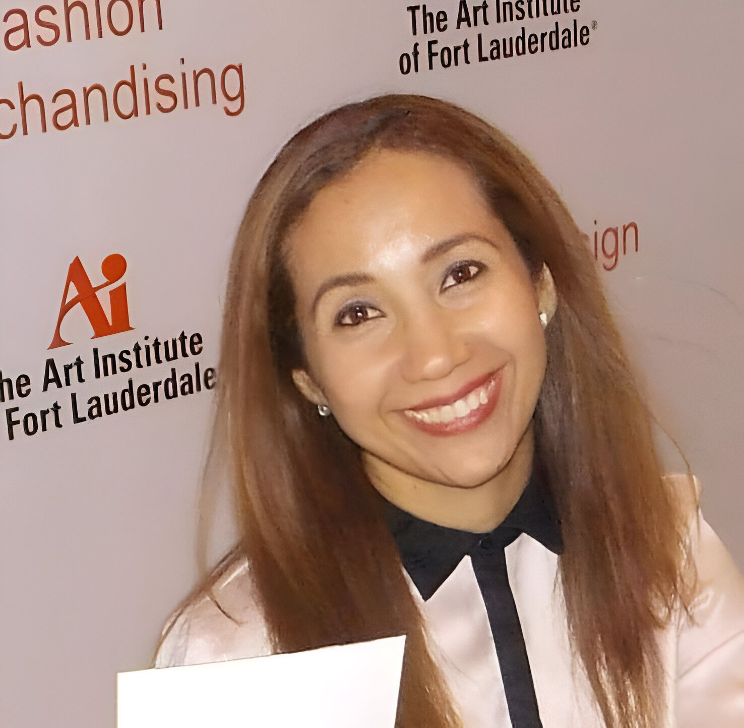 Mujer sonriendo, vistiendo una blusa rosa claro con cuello negro, frente a un fondo del Instituto de Arte.