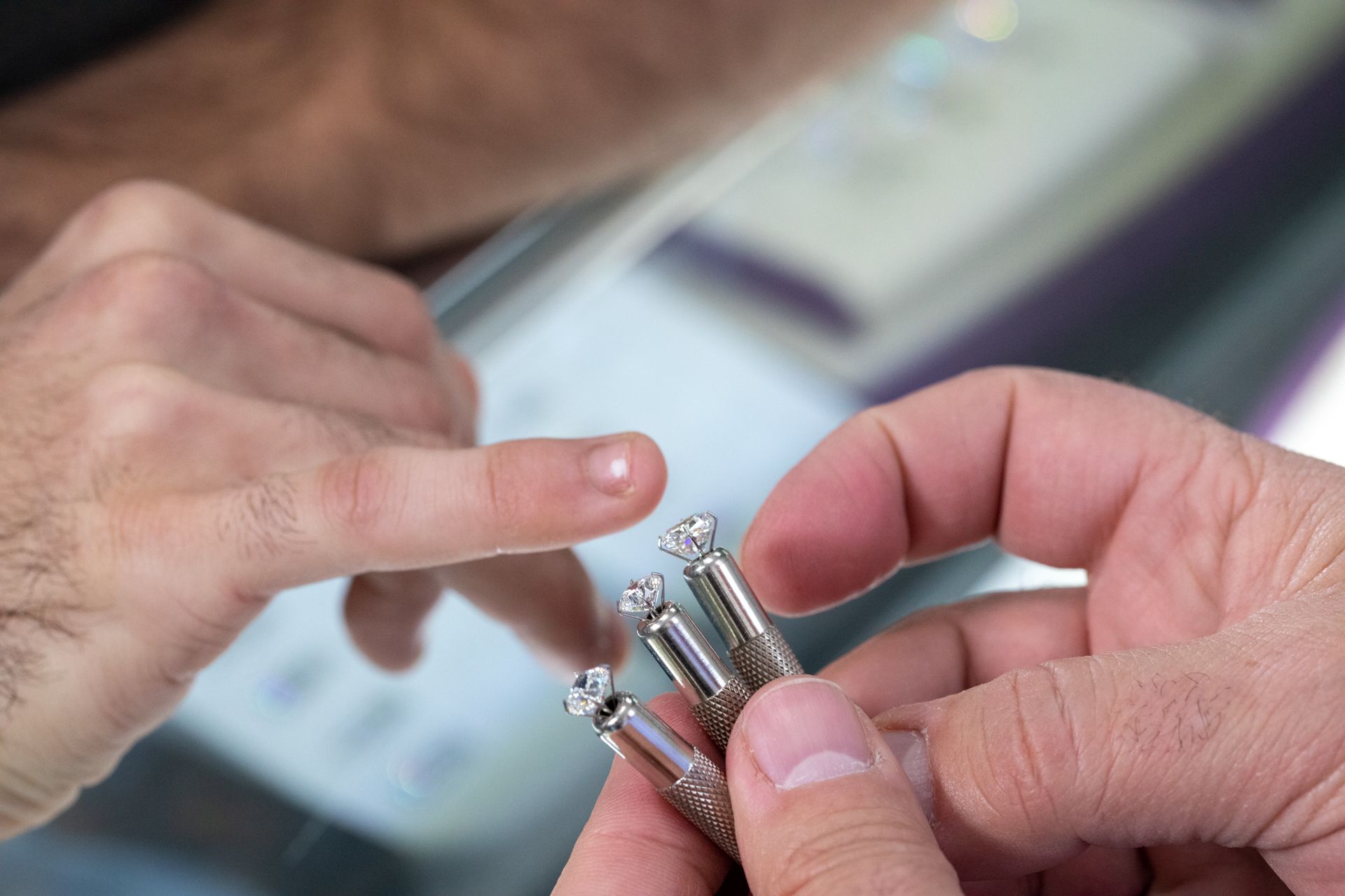 Hands compare a finger to several silver rings at a jewelry counter.
