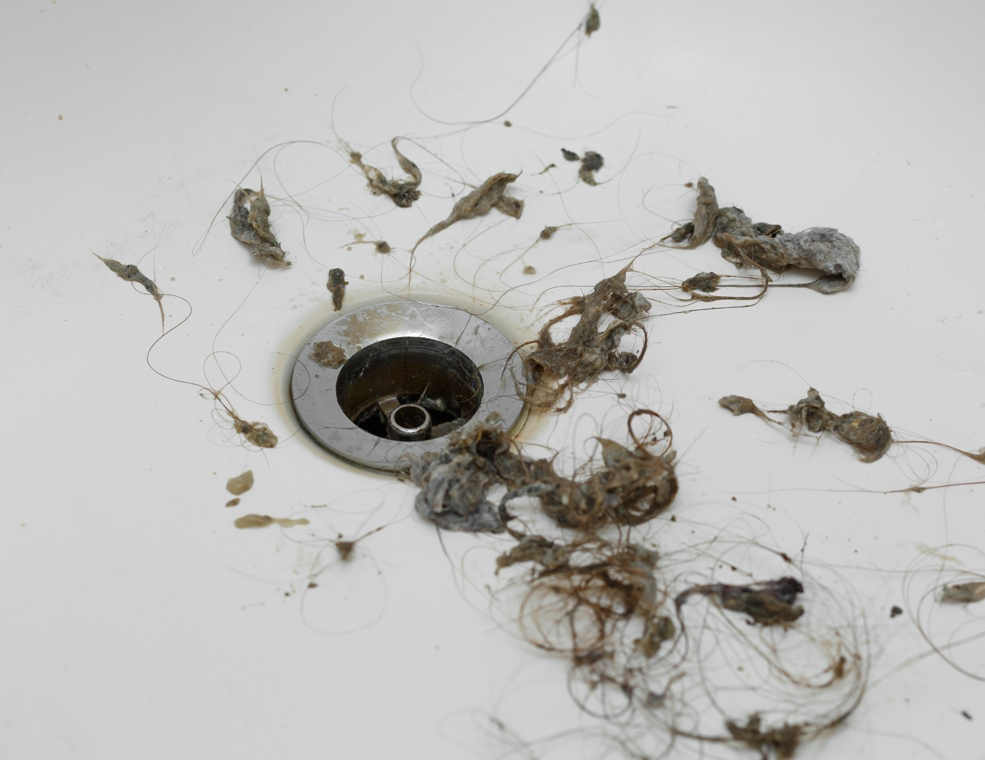 Dirty sink drain with clumps of hair and grime around the drain opening