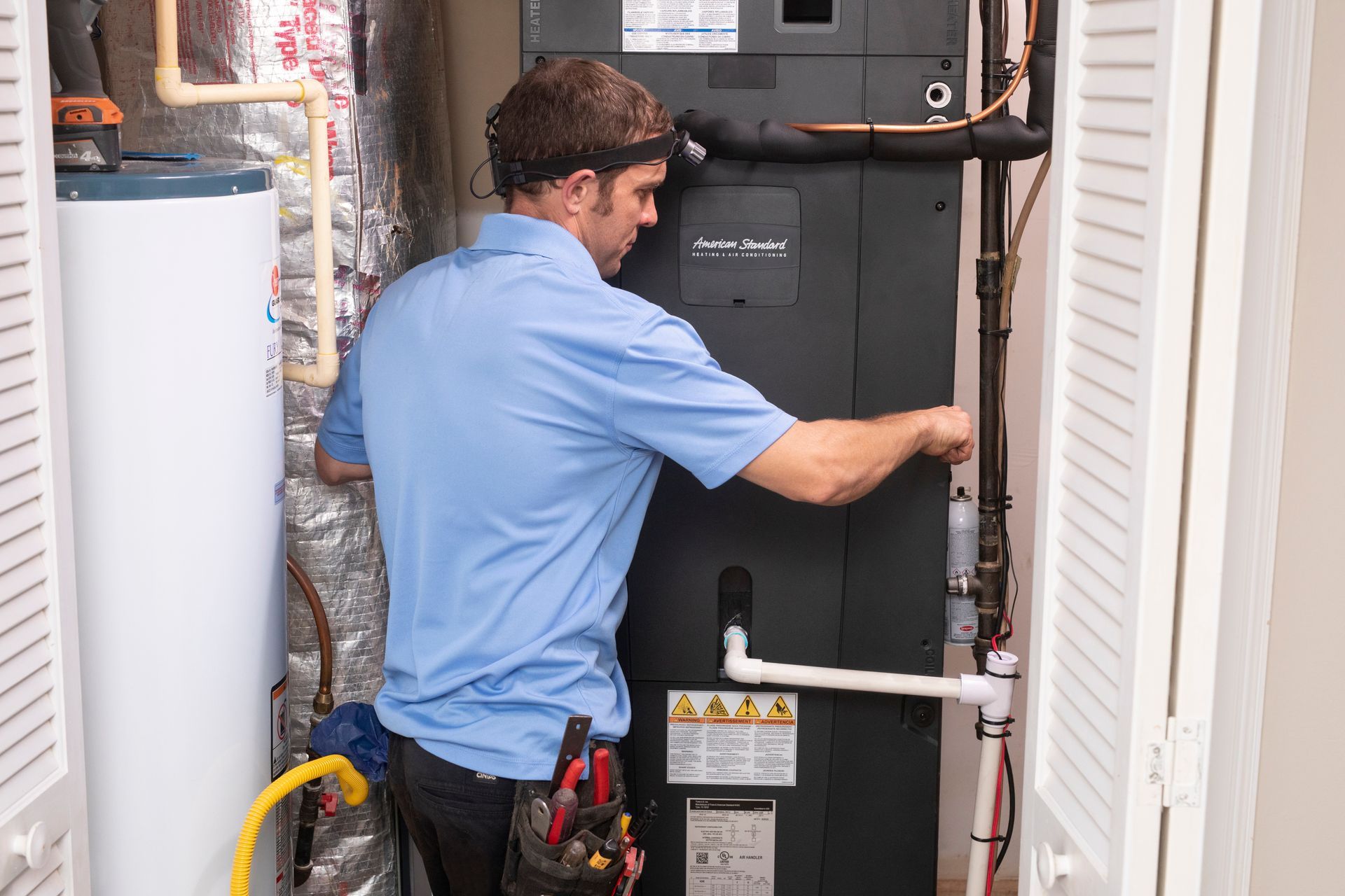 Technician inspecting a home HVAC unit in a utility closet.