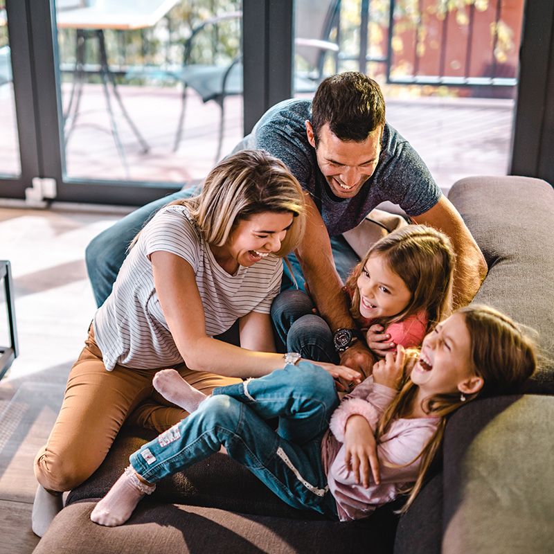Family laughing and playfully piling together on a couch in a bright living room