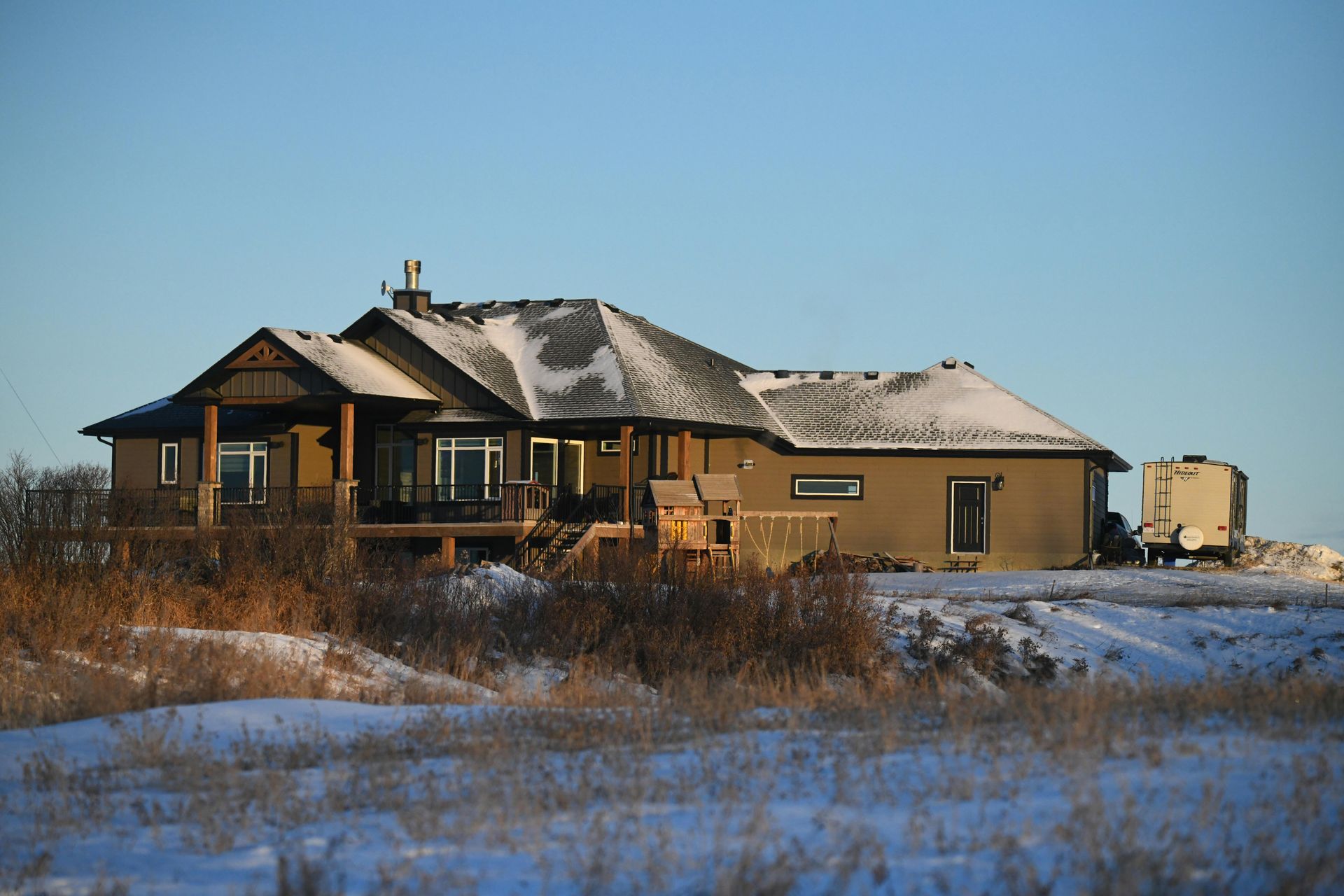Snowy house under construction in a rural field, with a clear blue sky and patches of snow on the roof