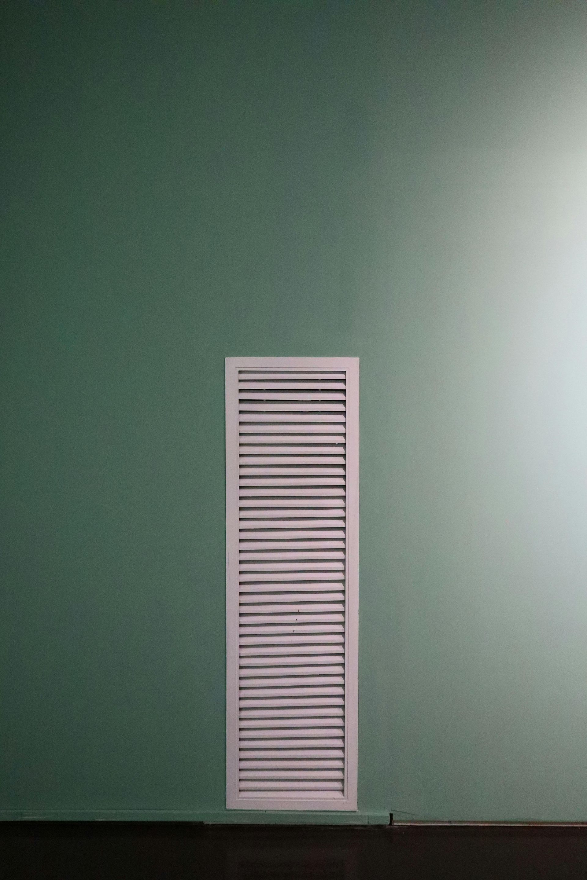 White wall vent on a green wall above a baseboard.