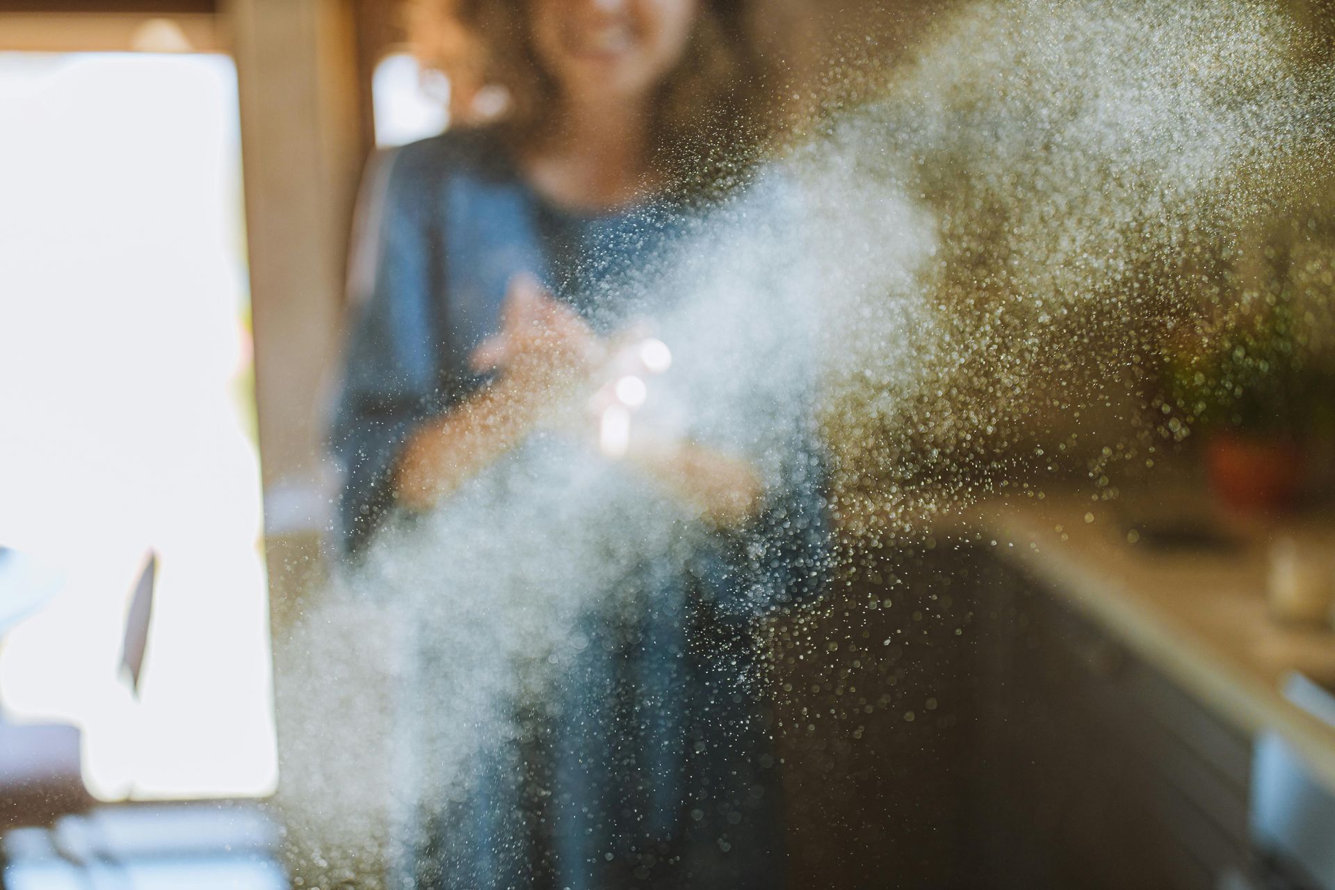Person spraying a cloud of disinfectant indoors near a sunlit window
