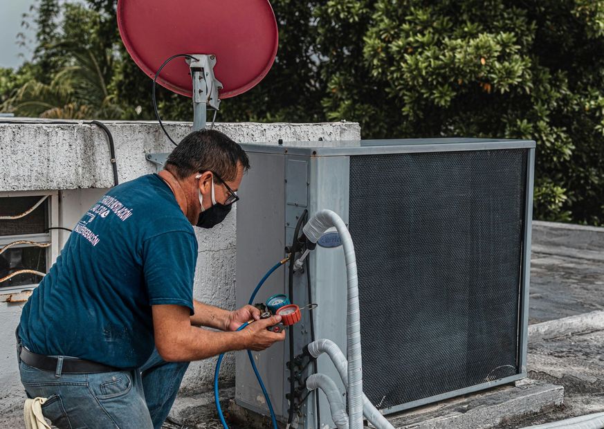 Technician servicing rooftop HVAC unit beside a red satellite dish under trees