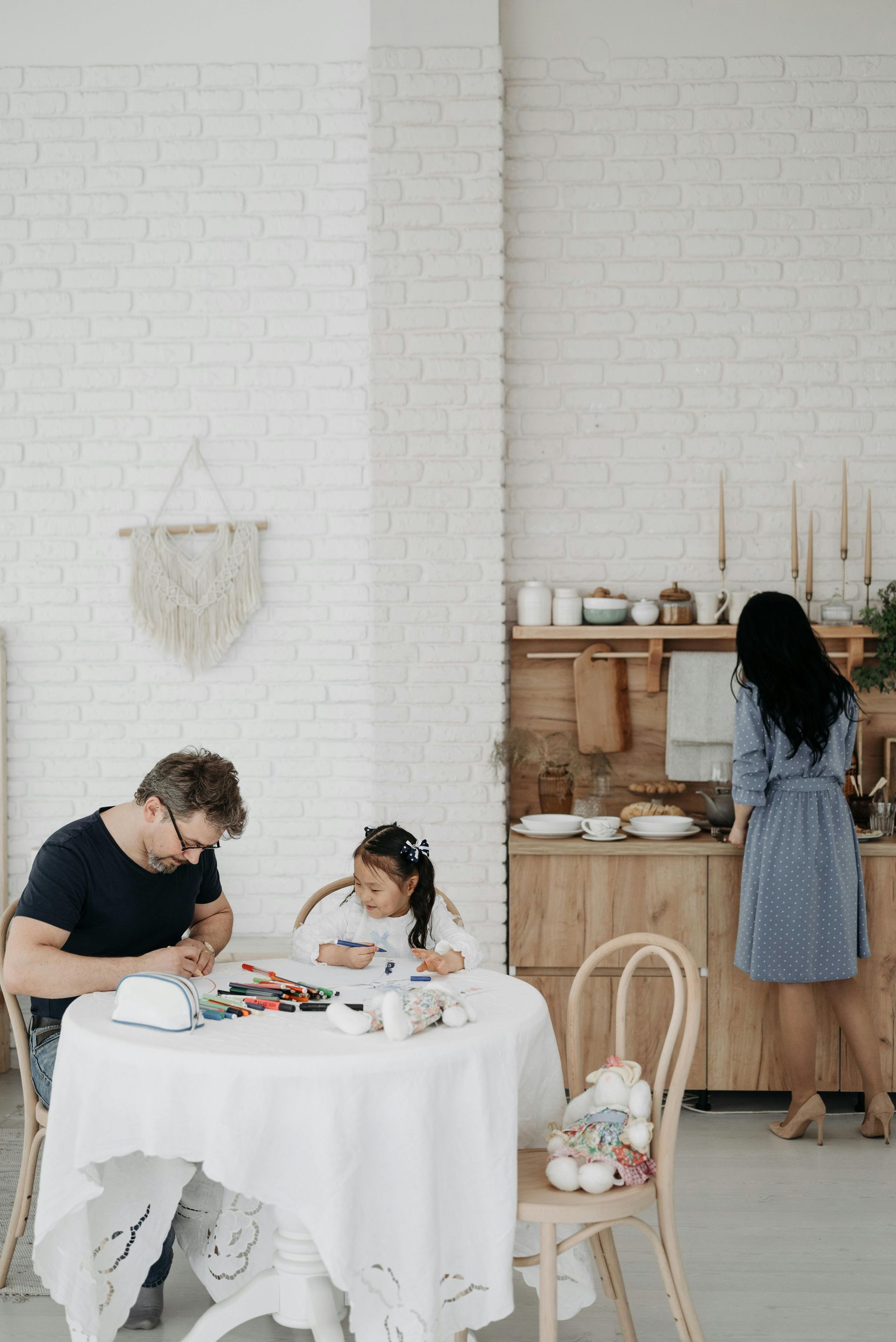 Family dining in a bright kitchen: two people at a white table while another prepares food at the counter