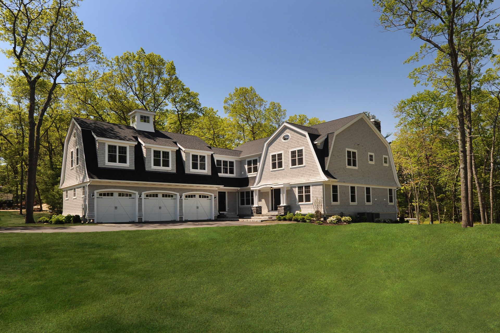 A large house with three garage doors is surrounded by trees