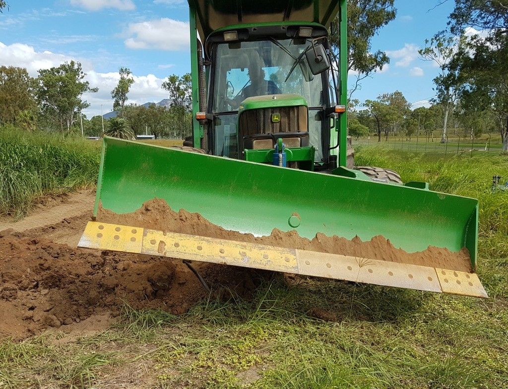 A green tractor is plowing a dirt road in a field.