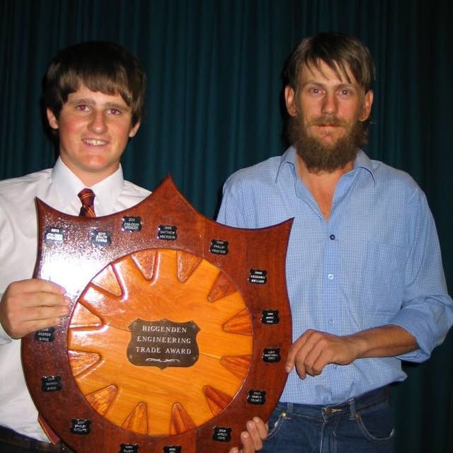 Two men are holding a wooden plaque that says trade award