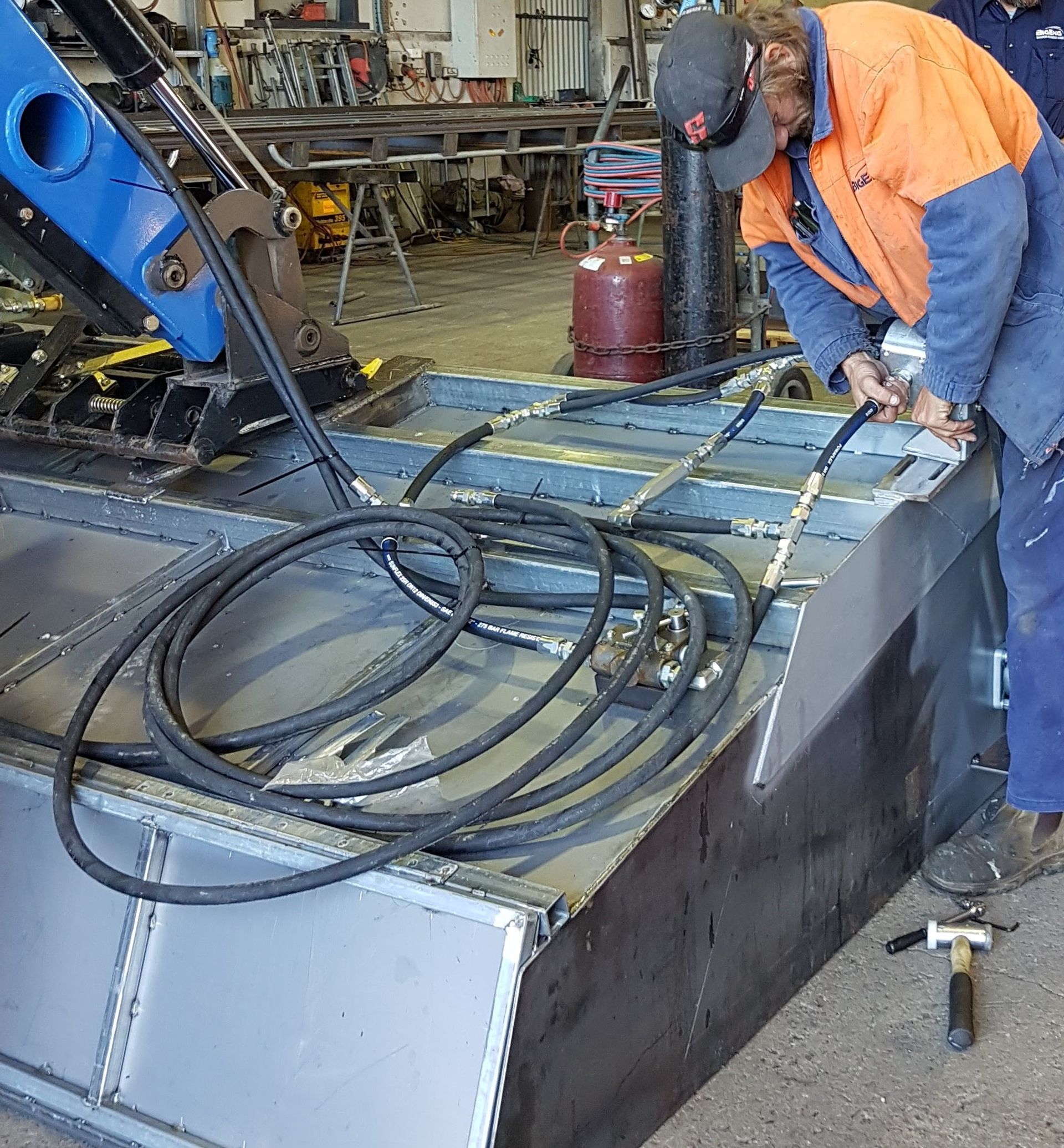 A man in an orange vest is working on a piece of metal