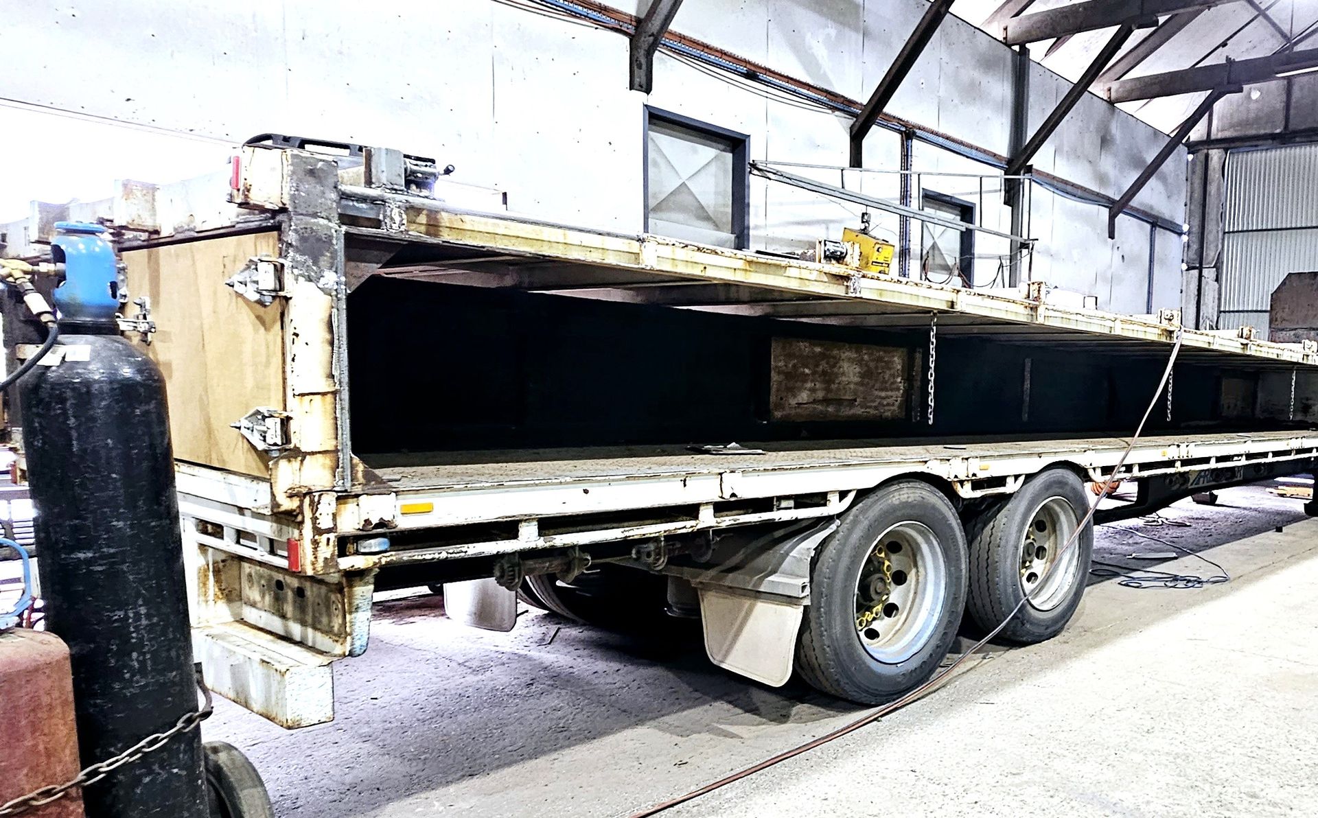 A flatbed truck is parked in a warehouse next to a gas cylinder.