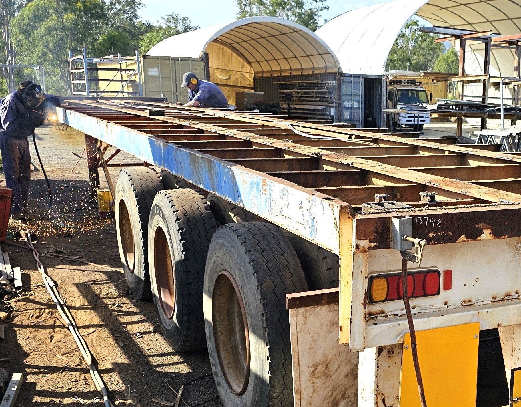 A man is welding a trailer in a parking lot