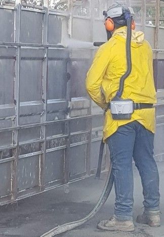 A man in a yellow jacket is spraying a wall with a hose.