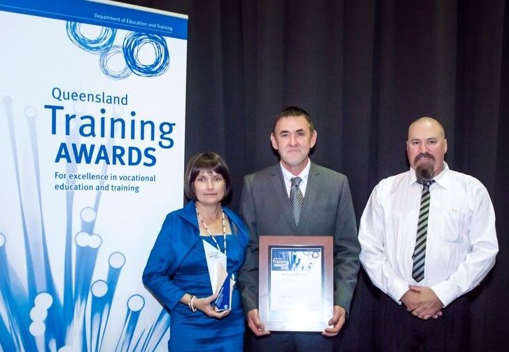 Three people are standing in front of a sign that says queensland training awards