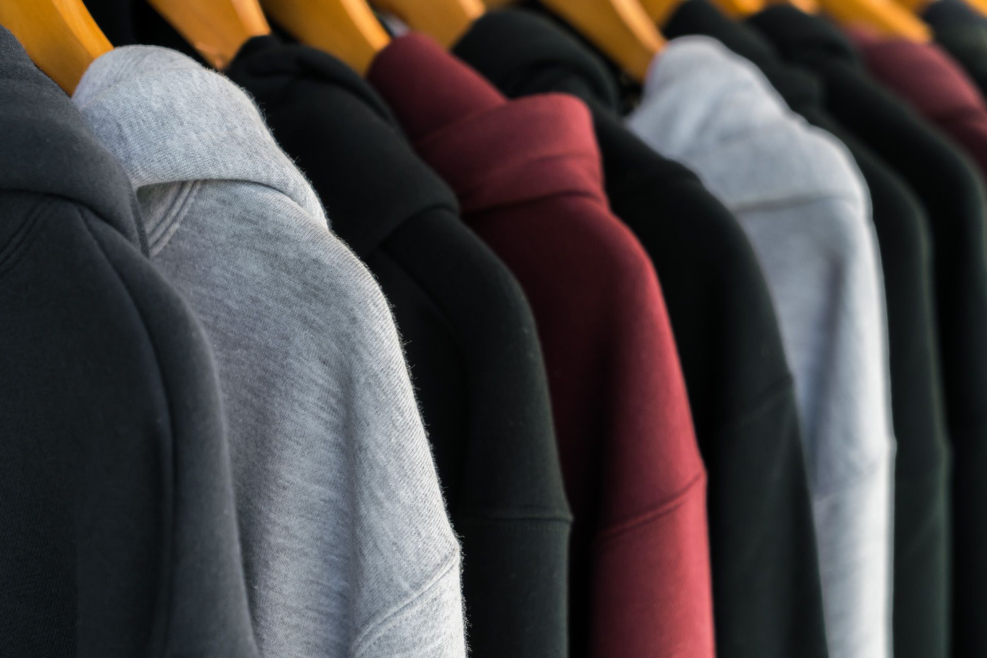 Una fila de sudaderas con capucha de diferentes colores están colgadas en un estante.