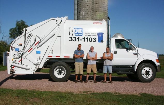 Three men are standing in front of a garbage truck with the number 331-1103 on it