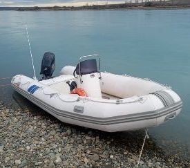 Un bote inflable blanco con motor está sentado en la orilla de un lago.