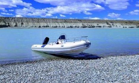 Un bote inflable blanco con motor está sentado en la orilla de un lago.