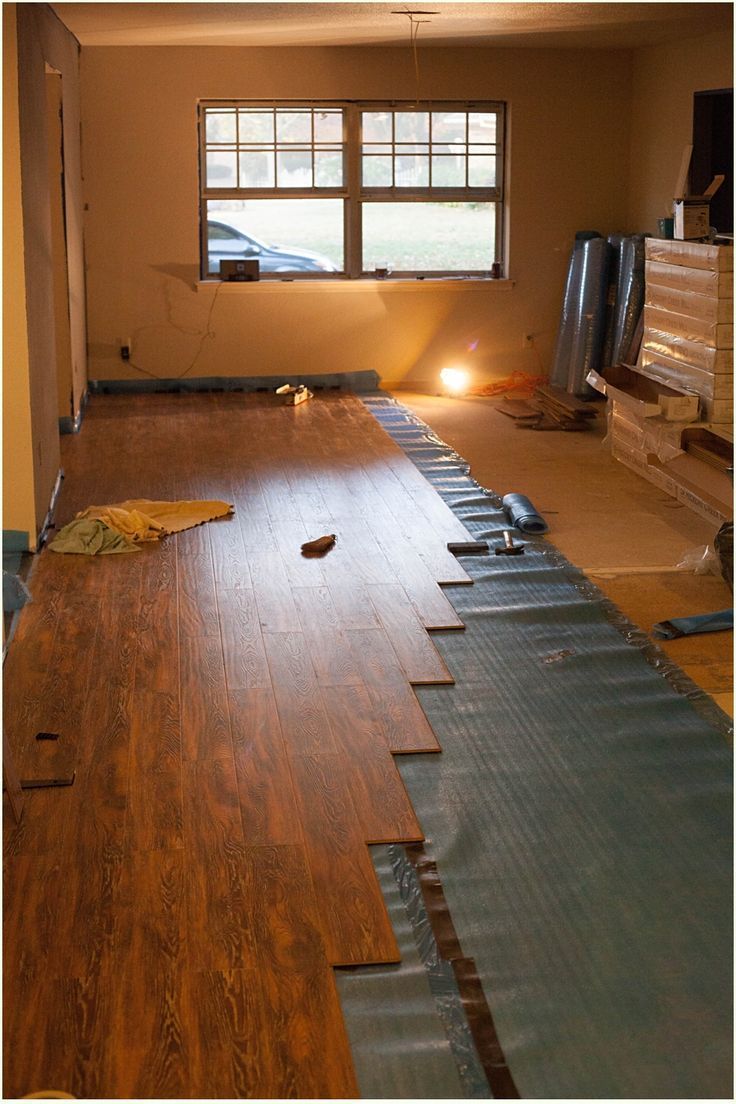 A room under renovation with partially installed wood-look laminate flooring over a blue underlayment.