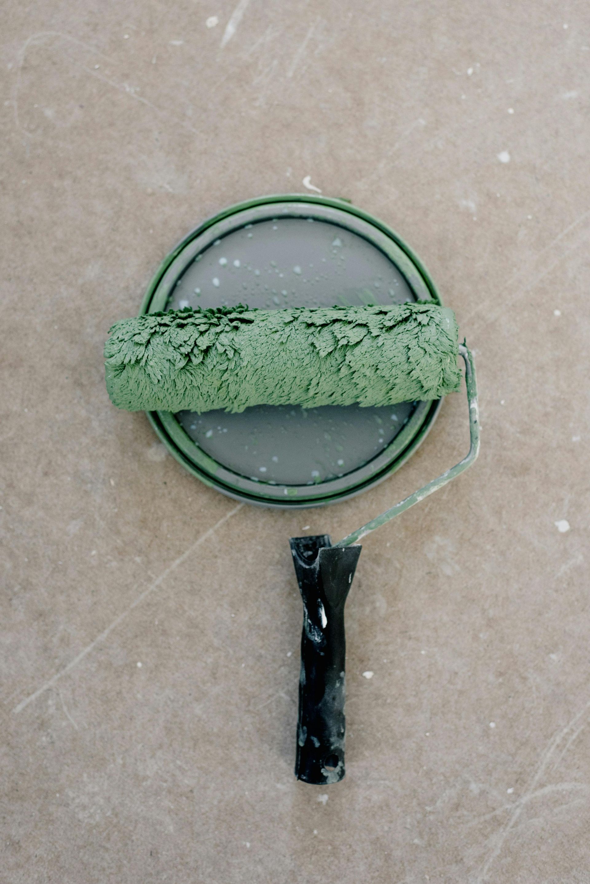 A green paint-covered roller lying horizontally on top of a circular paint can lid.