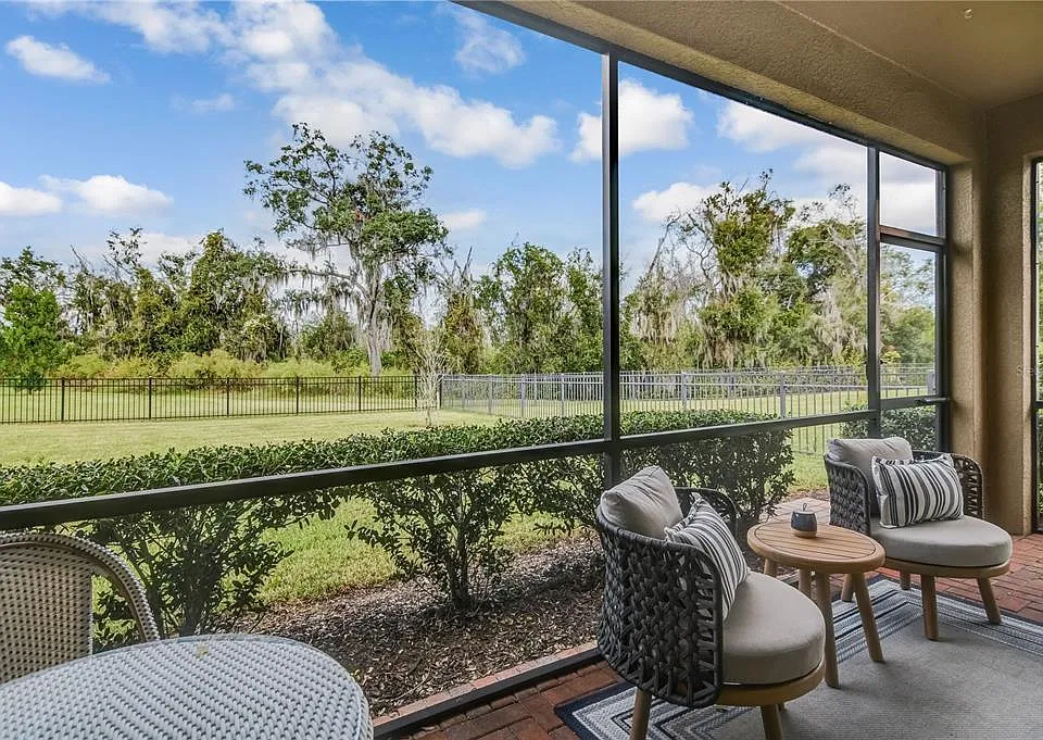 Screened-in patio with two armchairs and a small table overlooking a grassy yard with trees and a fence.