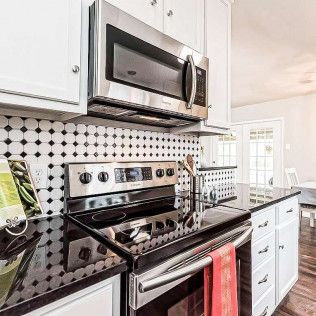 Modern kitchen with white cabinets, black countertops, stainless steel appliances, and a black and white tiled backsplash.