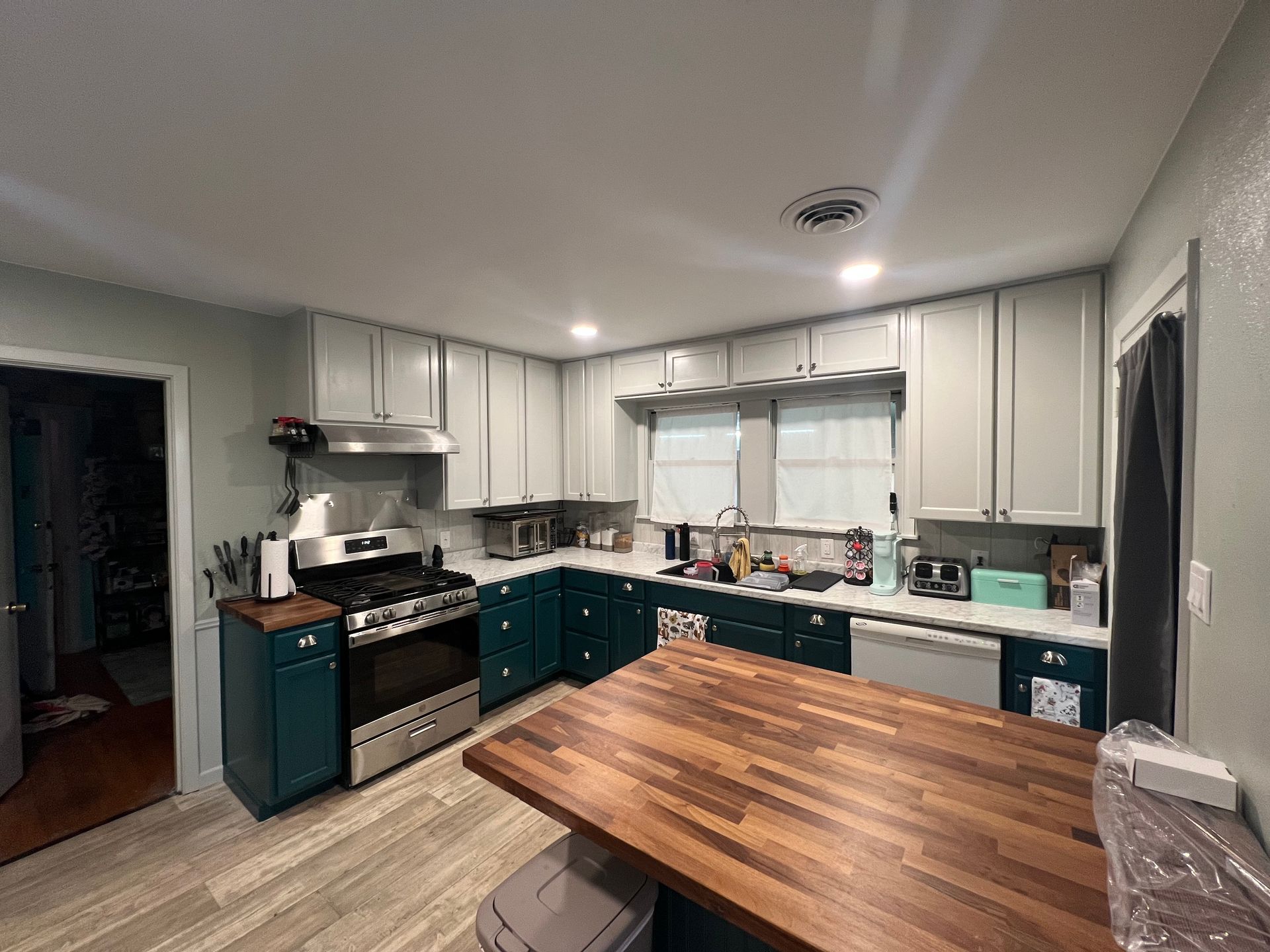 A kitchen with gray upper cabinets, teal lower cabinets, and a butcher block island. Appliances are stainless steel.