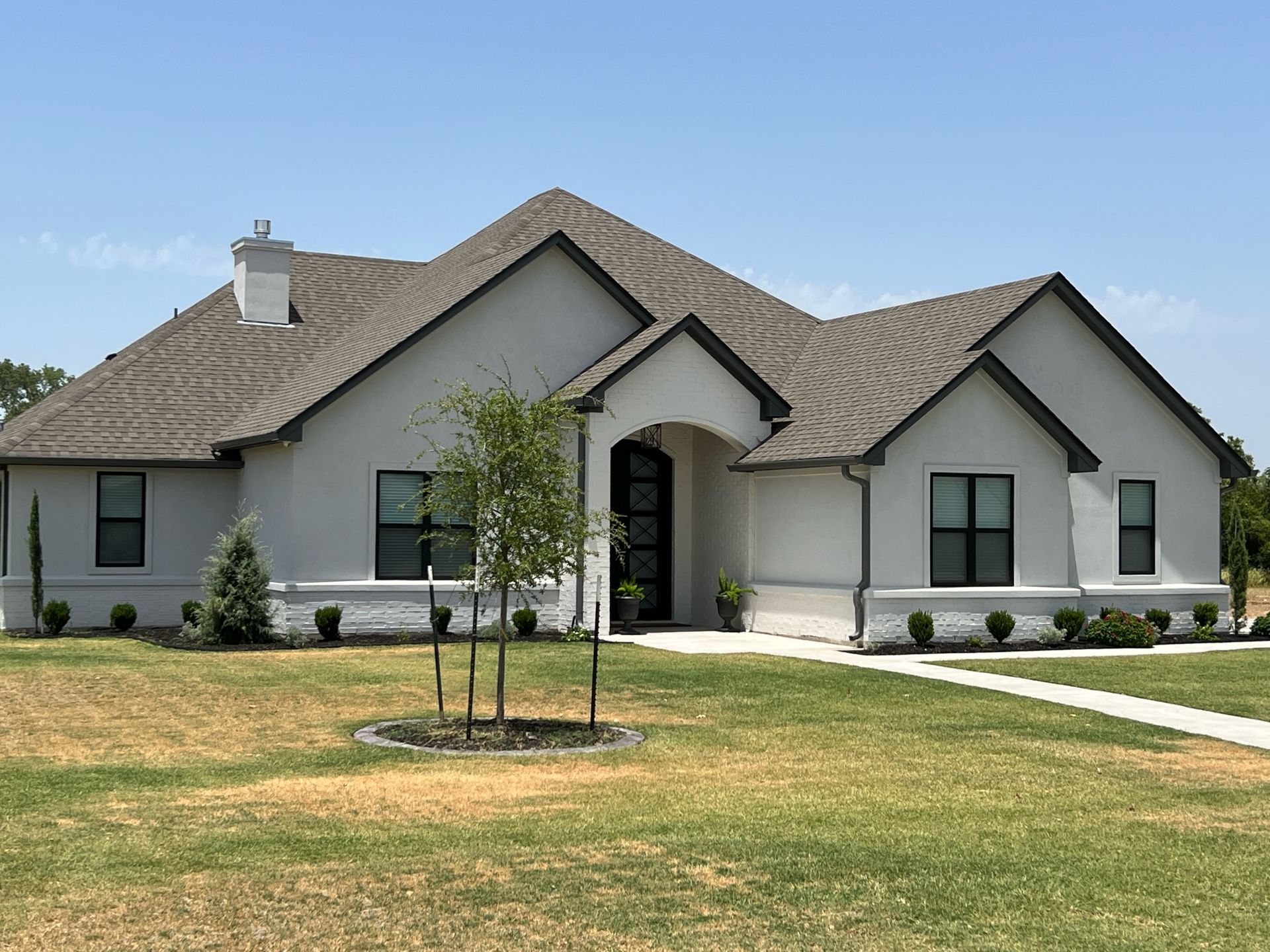A single-story house with stone facade, black trim, and a pathway leading to the front door. A mailbox stands at the start of the pathway.