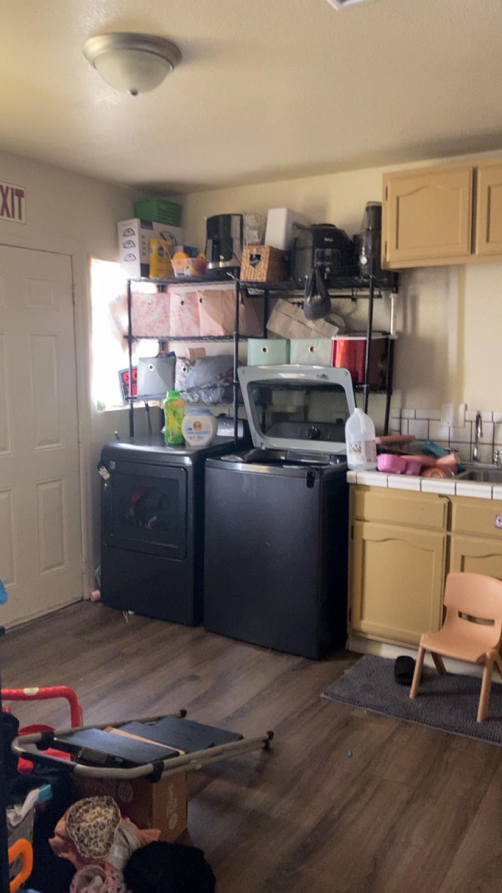 Laundry room with a washing machine and dryer, storage shelves, and cabinets. A child's chair sits near a sink.