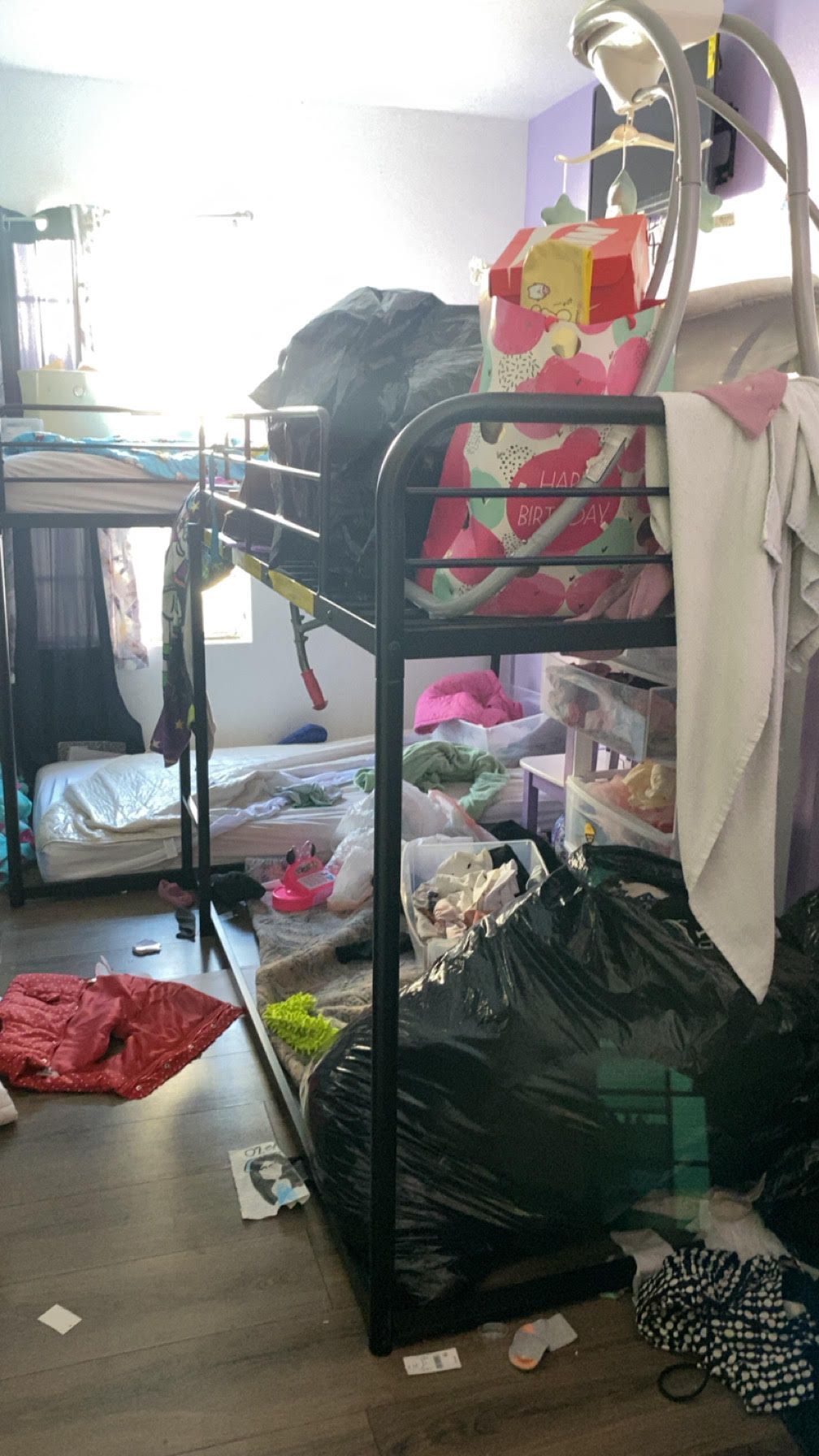 A cluttered room with two sets of bunk beds. The beds are filled with clothes, trash, and other items.