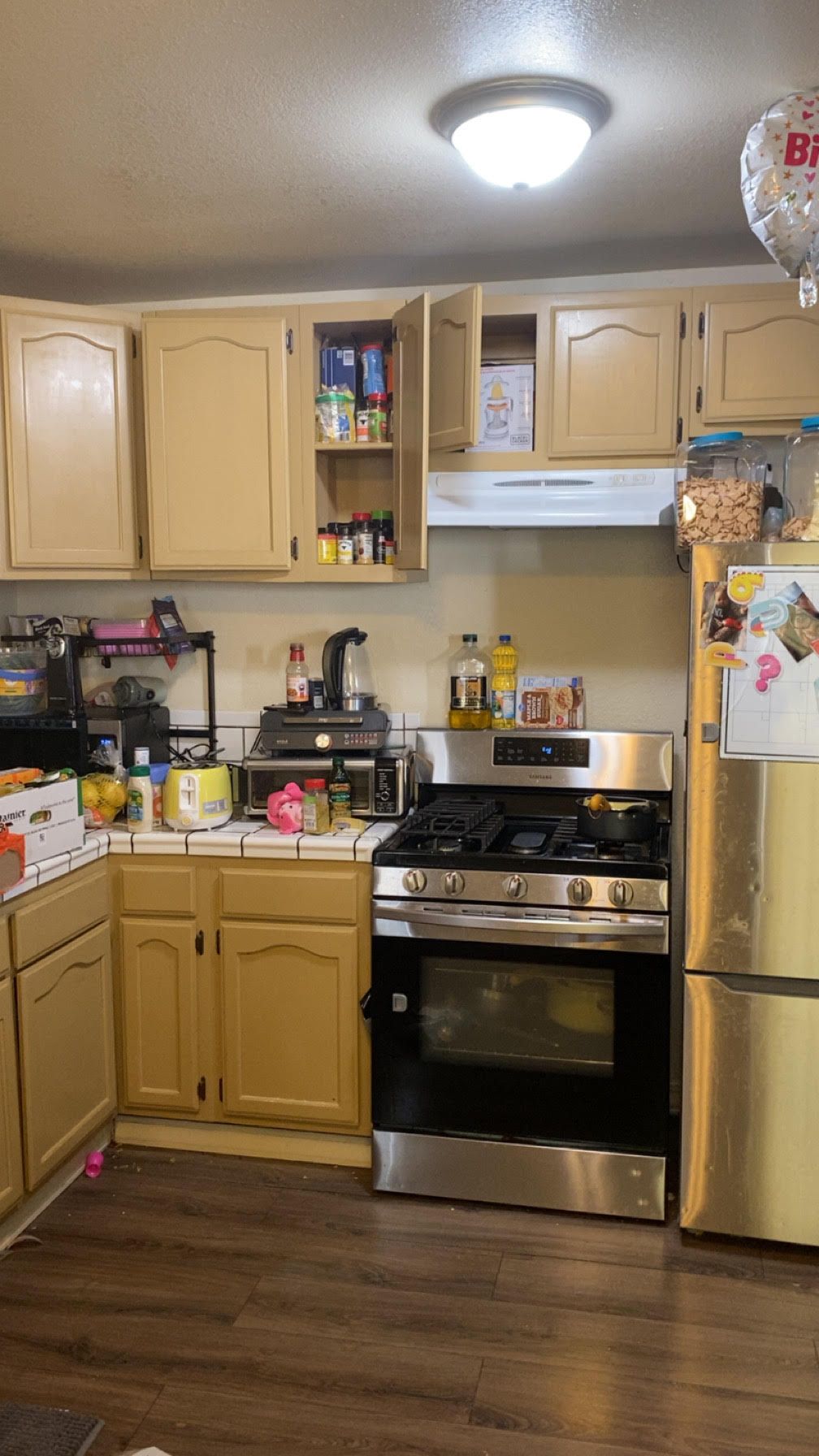 A kitchen with tan cabinets, a stainless steel stove, and a refrigerator.