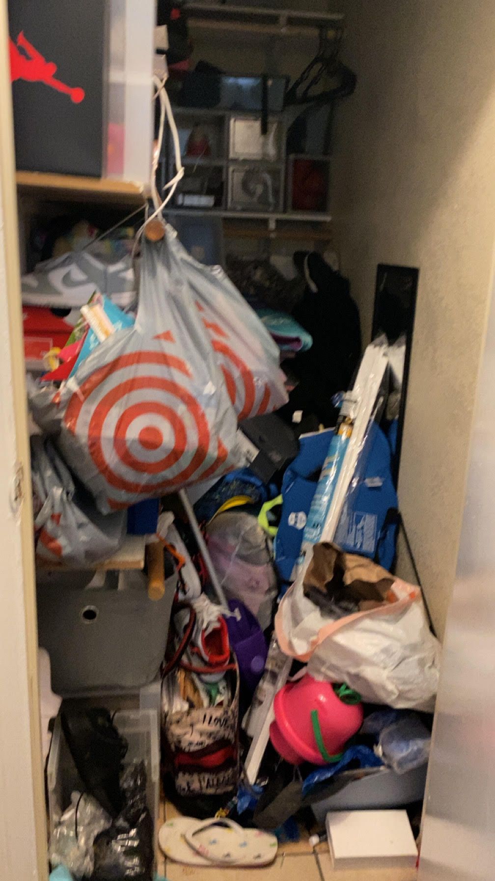 Cluttered closet filled with various items, including bags, bins, shoes, and other household objects.