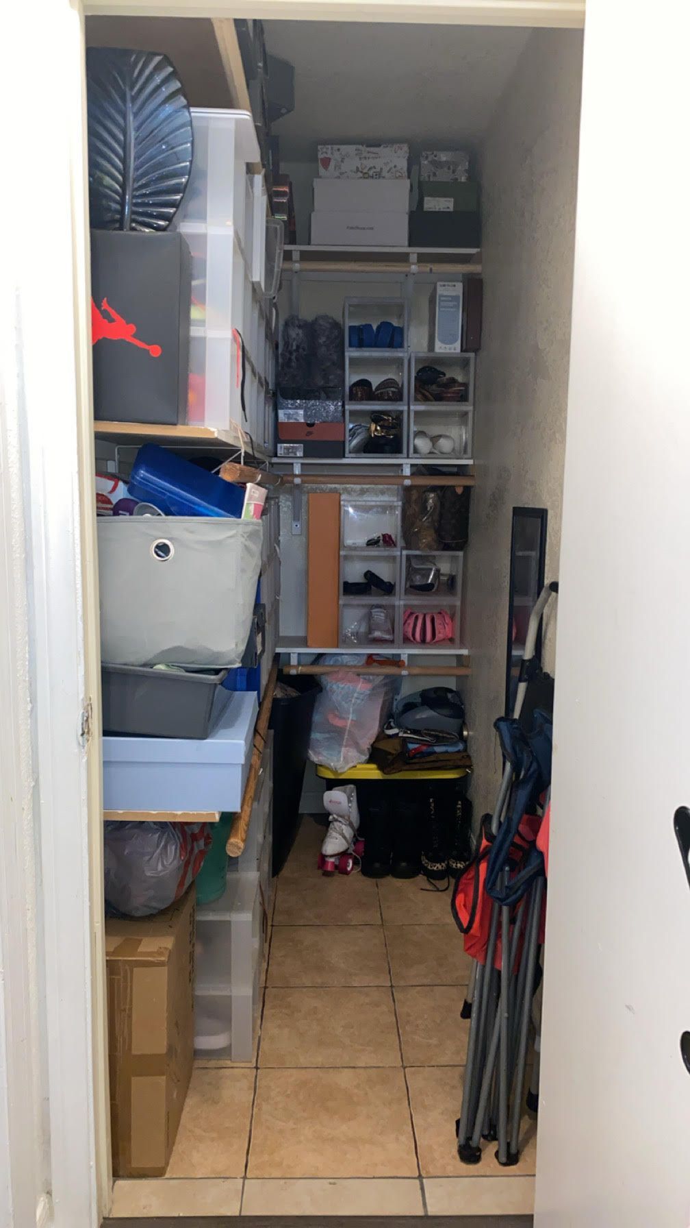 A narrow, cluttered closet with multiple shelves filled with shoes, boxes, and various items.