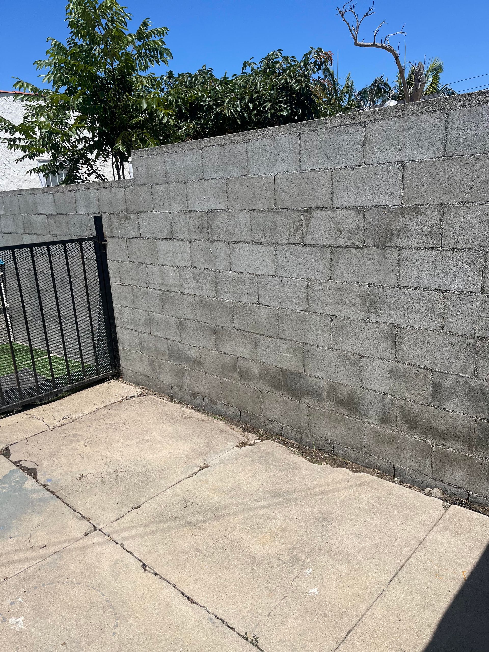Concrete block wall and patio with a wrought iron gate, under a clear blue sky.