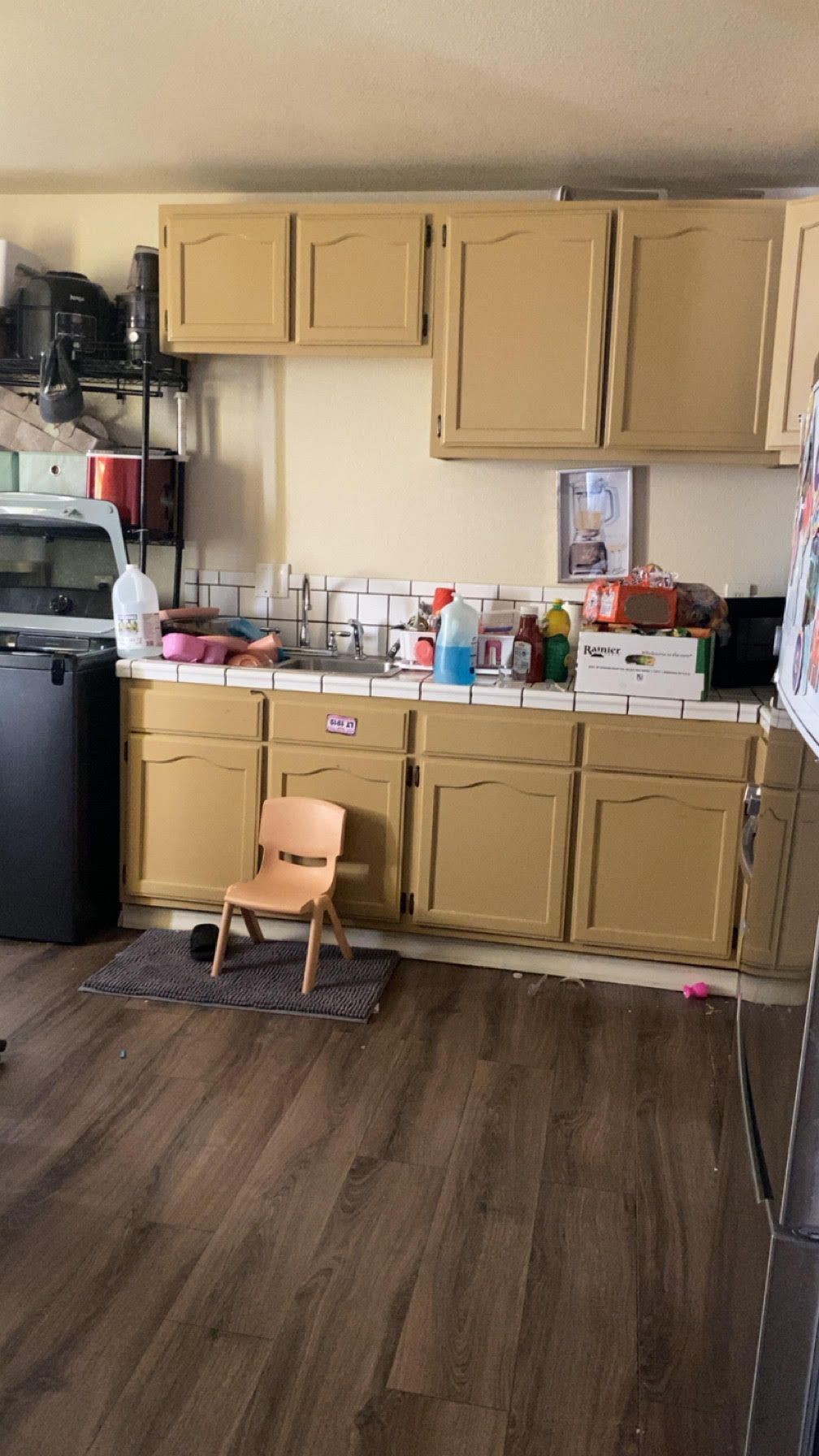 A cluttered kitchen with tan cabinets and a small wooden chair.
