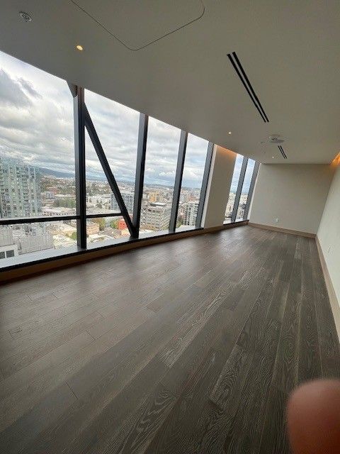 An empty room with dark wood flooring and floor-to-ceiling windows showing a city view. An empty room with dark wood flooring and floor-to-ceiling windows showing a city view.