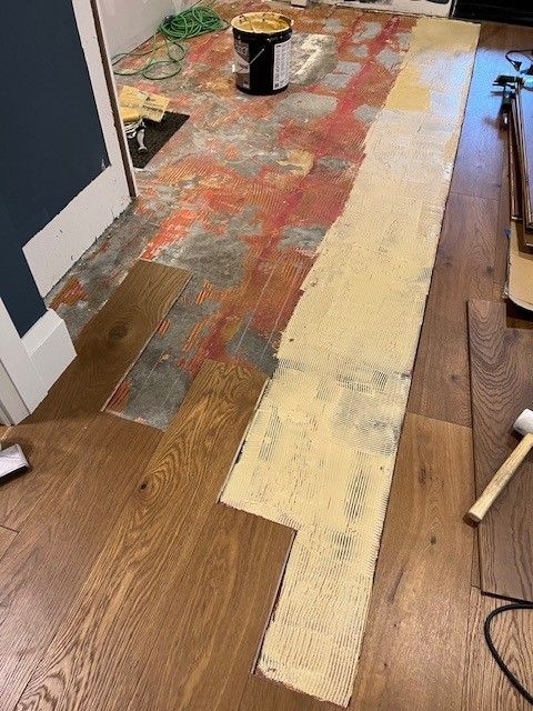 Wood planks are being glued to a floor with adhesive, showing the ongoing installation process in a room. Wood planks are being glued to a floor with adhesive, showing the ongoing installation process in a room.