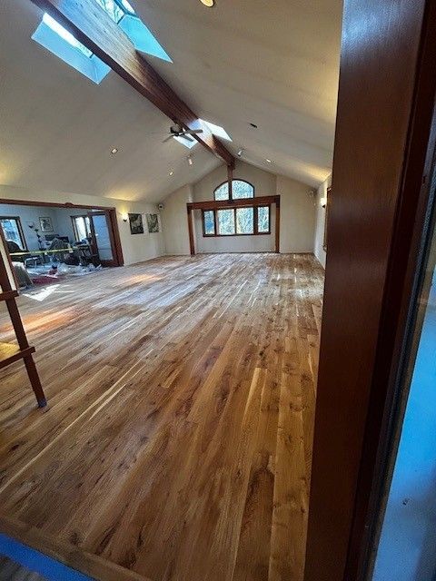 A spacious, sunlit room featuring warm-toned wooden floors, vaulted ceilings with exposed beams, and a large arched window. A spacious, sunlit room featuring warm-toned wooden floors, vaulted ceilings with exposed beams, and a large arched window.