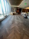 A modern, high-rise room with dark herringbone wood flooring, large floor-to-ceiling windows, and minimalist decor. A modern, high-rise room with dark herringbone wood flooring, large floor-to-ceiling windows, and minimalist decor.