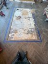 A rectangular section of parquet flooring has been removed, revealing the subfloor, outlined by blue painter's tape. A rectangular section of parquet flooring has been removed, revealing the subfloor, outlined by blue painter's tape.