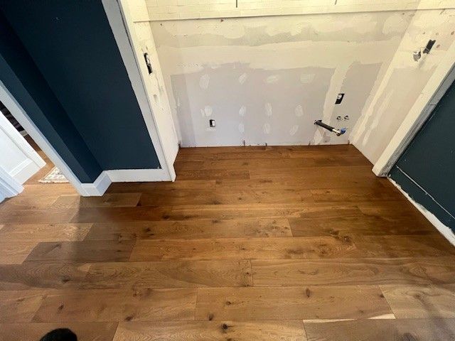 A room featuring dark blue walls, baseboard trim, and newly installed wide-plank wood flooring in front of a drywall area. A room featuring dark blue walls, baseboard trim, and newly installed wide-plank wood flooring in front of a drywall area.